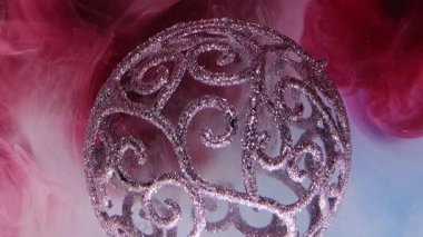 Parlak süs. Boya suyu sıçraması. Odaklanamayan, parlak, mor, pembe Noel süsleri dumanlı bulutların soyut arka planında..