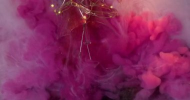 Duman sıçrıyor. Sis dalgası. Pembe akarsu boyası, siyah arka planda beyaz peçeyi karıştırıyor. Değişen parıldayan sanatsal sıvı cam kırıkları ampulü yakar.