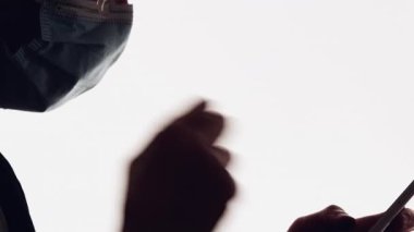 Salgın muhabbeti. Karantina devrede. Beyaz fotokopi arkaplanında izole edilmiş telefon kullanarak öksürük maskeli hasta adamın karanlık profilli silueti..