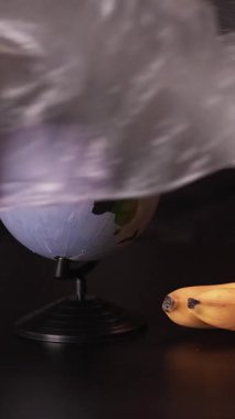 Dikey video. Plastik kirliliği. Doğa koruma. Ekoloji koruması. Dünyayı kaplayan polietilen film koyu renkli taze organik meyve kompozisyonu ile.