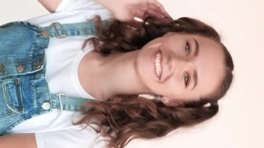 Dikey video. Neşeli ergen portresi. Gençlik yaşam tarzı. Dertsiz, eğlenceli, olumlu duygu. Beyaz arka planda sırıtarak oynayan iki at kuyruklu neşeli kız..