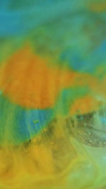 Dikey video. Mürekkep girdaplı su. Gradyan boya. Odaklanmamış mavi turuncu yeşil renk parlak sıvı parıltı emülsiyon akan su dokusu soyut sanat arka planı.