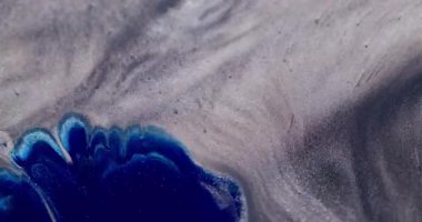 Mürekkep lekesi. Parıltı karışımı. Parlak mavi lekeli sıvı gümüş gri parıldayan parçacıkların yüzeyine yayılmış. Kontrast rengi soyut odaklanmış arkaplan.