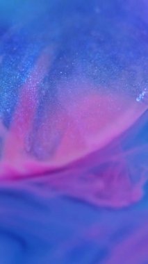 Dikey video. Parlak mürekkep. Boya karışımı. Işıl ışıl parlıyor. Odaklanmamış mavi mor renkli kıvrımlı dumanlı partiküller ıslak dokular soyut sanat arka planı.