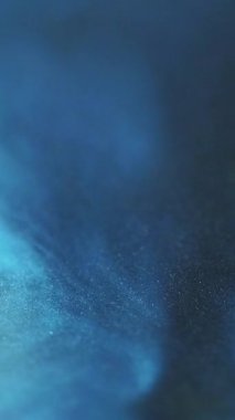 Dikey video. Odaklanmamış sim. Işıldayan arka plan. Mavi parlak emülsiyon. Parlak parçacıklar. Sıvı boya dalgası..