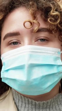 Dikey video. Karantina yüzü. Salgın hayat. Hava kirliliği. Enfeksiyon önleme. Koruyucu tıbbi maskeli, üzgün, umut dolu gözleri olan bir kadının yakın plan portresi..