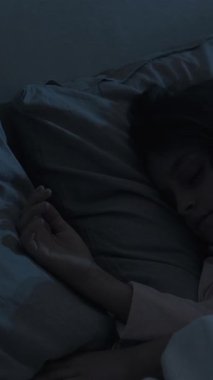 Dikey video. Uyuyan çocuk. İyi geceler. Tatlı rüyalar. Rahat, huzurlu küçük bir kız. Rahat bir yatakta uzanıyor. Evdeki karanlık yatak odasında, mavi ay ışığında..