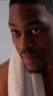 Dikey video. Cilt nemlendirici. Erkek bakım kozmetik ürünü. Beyaz havluyla duştan sonra yüz kremi süren kendine güvenen adam..