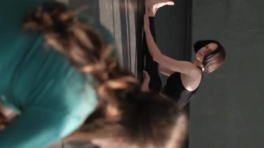 Dikey video. Esneme stüdyosu. Pilates egzersizi. Grup üyeleri spor salonundaki spor minderi üzerindeki kadın yoga eğitmeninden sonra jimnastik sınıfı egzersizlerini tekrarlıyor..