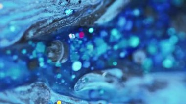 Dikey video. Parlak sıvı dökülmüş. Parlak mürekkep dokusu. Bulanık mavi, parlak pullu pullu parçacıklar akrilik boya, sıvı damlalar, soyut sanat arka planı, bokeh ışıkları..