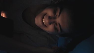 Dikey video. Gece sohbeti. Geç iletişim. Çevrimiçi boş zaman. Mutlu şakacı kadın mesajlaşır mesajlaşır. Karanlık odada cep telefonuyla flört eder..