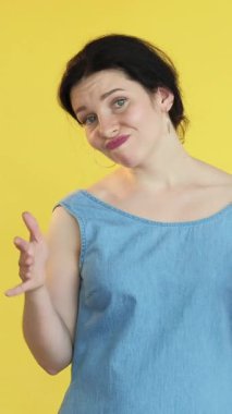 Dikey video. Şöyle böyle bir jest. Şüpheci bir ifade. Kadın emin değil belirsizlik sinyali çift duygu el hareketi yüz ifadesi ile bilmiyor sarı serbest alan arka planı izole.