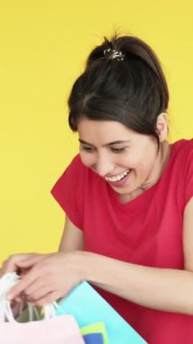Dikey video. Memnun edici alışveriş. Hediye terapisi. Heyecanlı mutlu kadın bir sürü kağıt torba alıyor neşeli müşteri sarı boş alanda izole edilmiş..