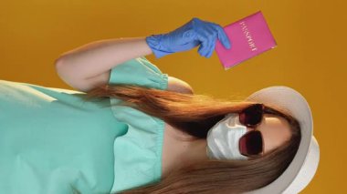 Dikey video. Küresel göç. Karantina kısıtlaması. Turist kadın koruyucu maskeli eldiven ve pasaport onaylı oturma izni turuncuyla izole edilmiş..