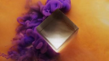 Duman akıntısı. Mürekkep atışı. Portakal rengi parıldayan sanat suyunda mor puf sprey cam küp. Renk karışımı ton bulanık arkaplan.