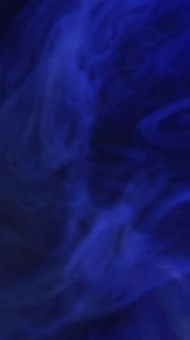 Dikey video. Bulanık sis bulutu. Boya suyu sıçraması. Odaklanmamış mavi renkli, parlayan toz parçacıkları koyu siyah soyut sanat arka planında yüzen sis dokusu..