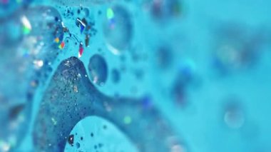Dikey video. Renk mürekkebi dökülmüş. Parlak yağ kabarcıkları. Odaklanmamış mavi renkli ışıldayan parçacıklar jel damlaları akrilik boya sıvısı parlatıcı doku akış hareketi soyut sanat arka planı.