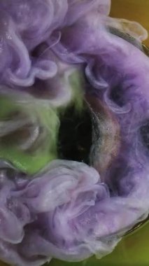 Dikey video. Boya patlaması. Renkli su. Mor parıltı akışı yeşil turuncu sis küre zaman yolculuğu gizemli siyah kristal soyut arka plan.