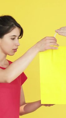 Dikey video. Neşelen biraz. Beklenmedik bir hediye. Şimdiki rüyayı gerçekleştiren kadın mutlu bir şekilde sarı boş alanda izole edilmiş alışveriş torbaları ile mutlu bir şekilde yaşıyor..