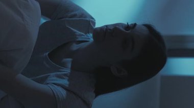 Dikey video. Gece endişesi. Uykusuzluk hastalığı. Yorgun, yalnız, depresif, uykulu, aşırı düşünen, iç çeken, karanlık yatak odasında geç saatlere kadar esneyen bir kadın..