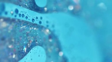 Dikey video. Parıltılı bir karışım. Akrilik boya dökülmüş. Bulanık mavi renk parlak pullu parçacıklar jel sıvısı yüzen kabarcıklar mürekkep emülsiyon sıvı akım hareket soyut sanat arka planı.