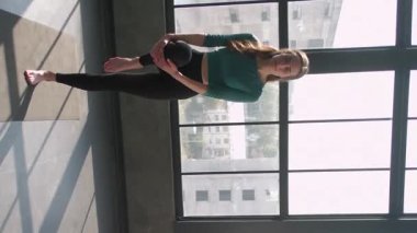 Dikey video. Yoga egzersizi. Eğlence egzersizi. Kadın spor eğitmeni eğitim grubu üyeleri Asana spor salonundaki spor salonunda bir bacak dengesi egzersizi yapıyor..