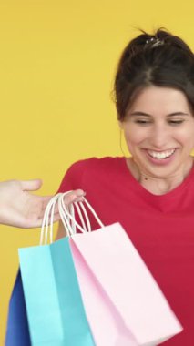 Dikey video. Tatmin edici bir sürpriz. Hediye terapisi. Bir sürü alışveriş çantası alan heyecanlı kadın mutlu, mutlu müşteri sarı boş alanda izole edilmiş..