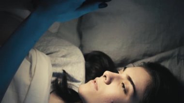 Dikey video. Gece online. Uyku zamanı aleti. Mobil uykusuzluk. Uykucu kız, internetten telefon kullanıyor internette geziniyor, geç saatlere kadar yatakta esniyor..