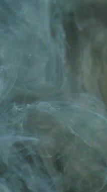 Dikey video. Işıltılı sis girdabı. Mürekkep su sıçratır. Odaklanmamış mavi altın rengi ışıldayan parçacıklar desen duman girdap hareketi soyut sanat arkaplanı.