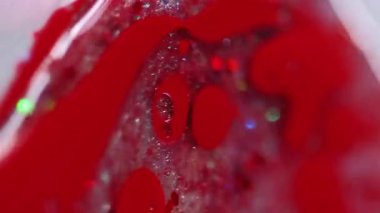 Dikey video. Sıvı pırıltı damlası. Parıltılı boya karışımı. Bulanık kırmızı renk parlak pullu parçacıklar mürekkep damlaları şeffaf jel sıvısı sızıntısı soyut sanat arka planı ve bokeh ışıkları.