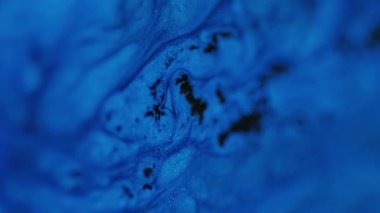 Damlayan ışıltılı doku. Akışkan sanat. Odaklanamayan mavi renkli parıldayan parçacıklar akrilik mürekkep dalgaları koyu soyut hipnotik gizemli uzay arkaplanı üzerinde hareket ediyor.