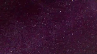 Parıltı etkisi. Bulanık toz parçacıkları. Işıl ışıl parlayan beyaz noktalar. Parlayan toz. Soyut mor arka planda dönen kıvrımlar..