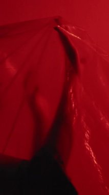Dikey video. Kadın özgürlüğü. Kadın hakları için. Koyu kırmızı üzerine saydam polietilen film sıkışmış korkmuş kız silueti..