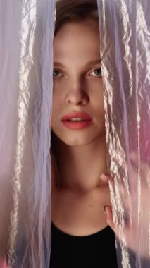 Dikey video. Kadın hakları savunucusu. Sinirli kadın. Pembe mavi renk gradyan parlaklığında buruşuk polietilen filmin arkasına saklanan rahatsız, güvensiz kız..