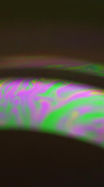 Dikey video. Renk karışımı. Psikedelik boya. Pembe, parlak, yeşil yağ kabarcığı sıvısı koyu siyah soyut sanat arka planında holografik eğri içinde harmanlanır..