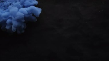 Duman boyası. Mistik duman. Siyah yüzeye mavi bulut spreyi döküldü. Suyun soyut arka planında renk üfürüğü bulanık pigment patlaması.