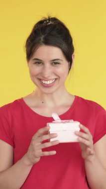 Dikey video. Beklenmedik bir hediye. Kadın hediye alıyor. Rüya tatmini. Mutlu bir mutluluk. Sarı arka planda izole edilmiş bir kutu..