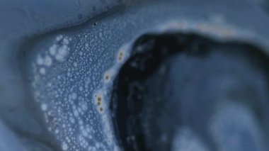 Parıltı yayılıyor. Boya damlası. Bulanık mavi, siyah, parlak, tahıl rengi, ıslak, mürekkep, su karışımı, soyut sanat arka planı..