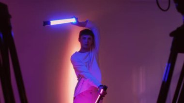 Fütürist stüdyo. Gece hayatı. Neon ışın kılıçları gibi LED tüpleri sallayan adam çok eğleniyor. Profesyonel ekipmanlarla video çekimi.