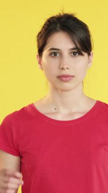 Dikey video. Neşeli bir ifade. İşaret parmağı. Heyecanlı mutlu kadın sarı arka planda izole edilmiş boş alana işaret ediyor..