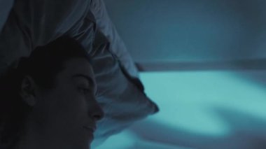 Dikey video. Gece yorgunluğu. Uyku sorunu. Yorgun, bunalımlı, yalnız bir kadın karanlık yatak odasında tavana bakıyor..