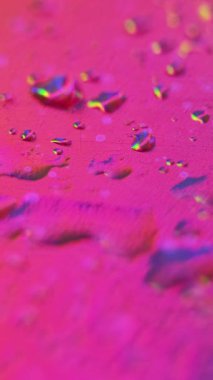 Dikey video. Gökkuşağı damlacıkları. Islak cam. Çizilmiş folyo folyolu film su yüzeyi soyut sanat arka planında odaksız renkli neon ışık hareketi.
