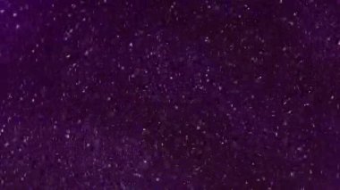 Görüntü pırıltısı. Yanıp sönen parçacıklar. Parlak beyaz renkler parıldıyor parlak parçalar fırıl fırıl dönüyor boya mürekkebi koyu mor soyut arka planda hareket ediyor.