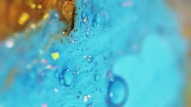 Dikey video. Mürekkep damlası. Parlak sıvı dokusu. Bulanık mavi altın rengi parlak metalik pullu parçacıklar yağ emülsiyonu boya döküntüsü soyut sanat arkaplanı Bokeh ışıkları.