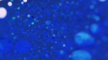 Dikey video. Sıvı sim damlası. Yağ sıvısı. Odaklanmamış mavi renk parçacıkları parıldayan boya damlaları pigment su mürekkebi emülsiyon hareket soyut sanat arka planı.