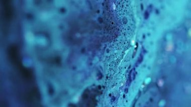 Dikey video. Parıldayan sıvı dökülmüş. Renk köpüğü dokusu. Odaklanmamış mavi ışıldayan pullu partiküller yağ kabarcıkları akrilik boya mürekkebi emülsiyon sıvı akış hareketi soyut sanat arka planı.