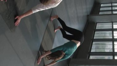 Dikey video. Pilates sporu. Yoga asana. Grup üyeleri denge egzersizi yapıyor. Köpek pozu veriyor. Spor salonundaki paspasın üzerinde kadın fitness hocasıyla kas esneme dersi veriyor..