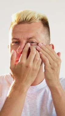 Dikey video. Göz bantları. Yaşlanma karşıtı tedavi. Kendine güvenen sarışın adam, temiz taze yüz derisine nemlendirici kollajen hidrojel pedleri uyguluyor..