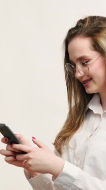 Dikey video. Dostça bir sohbet. Çevrimiçi iletişim. Gözlüklü, neşeli iş kadını. Telefonda mesaj okuyor. Gülüyor, gülüyor..