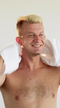 Dikey video. Duştan sonra sabah tazeliği. Beyaz banyodan sonra beyaz havluyla saçlarını silen mutlu, sarışın adam..